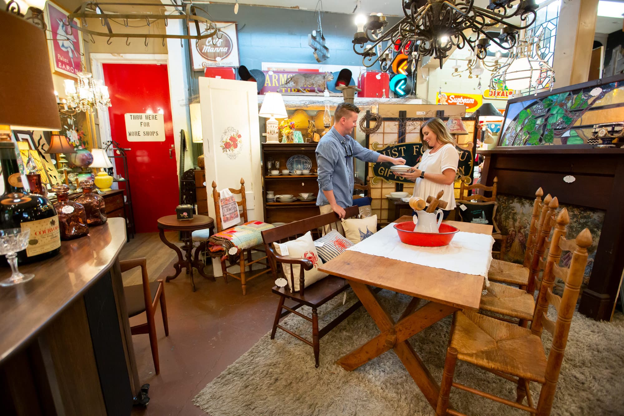 Couple looking at stoneware inside Dixieland Relics in Lakeland, FL. Home decor and antique furniture on display throughout room.