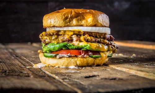 Hamburger with onion, cheese, lettuce, tomato, pickle and sauce on wooden table at Fire Restaurant in Winter Haven, FL