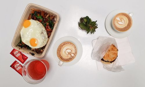 Food on white table. Vegan power bowl with two eggs, a chicken biscuit and Kombucha from Good Thyme LKLD. Two lattes from Concord Coffee.