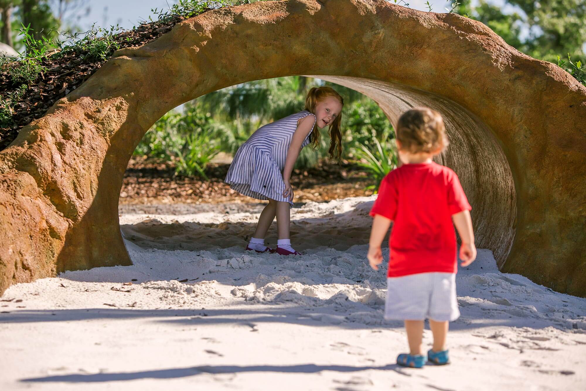 2 kids playing in Gopher Tortoise Burrow at Hammock Hollow in Bok Tower Gardens.