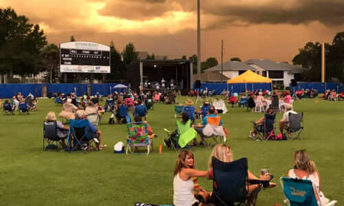 groups of people sitting outside at sunset during a concert at Chain O Lakes stadium